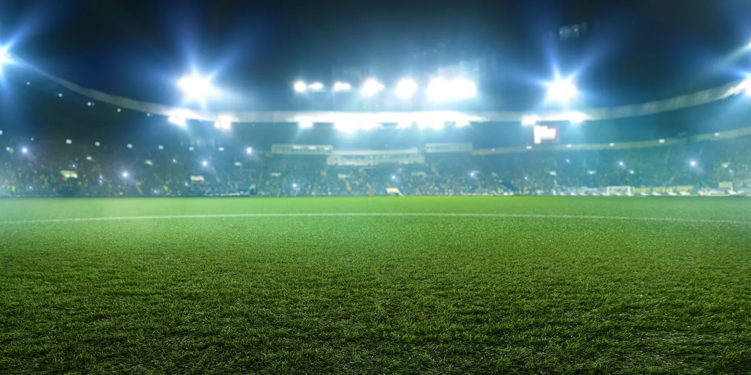 Fußballstadion mit gepflegtem Spielfeld und Tribüne voller Fans im Hintergrund